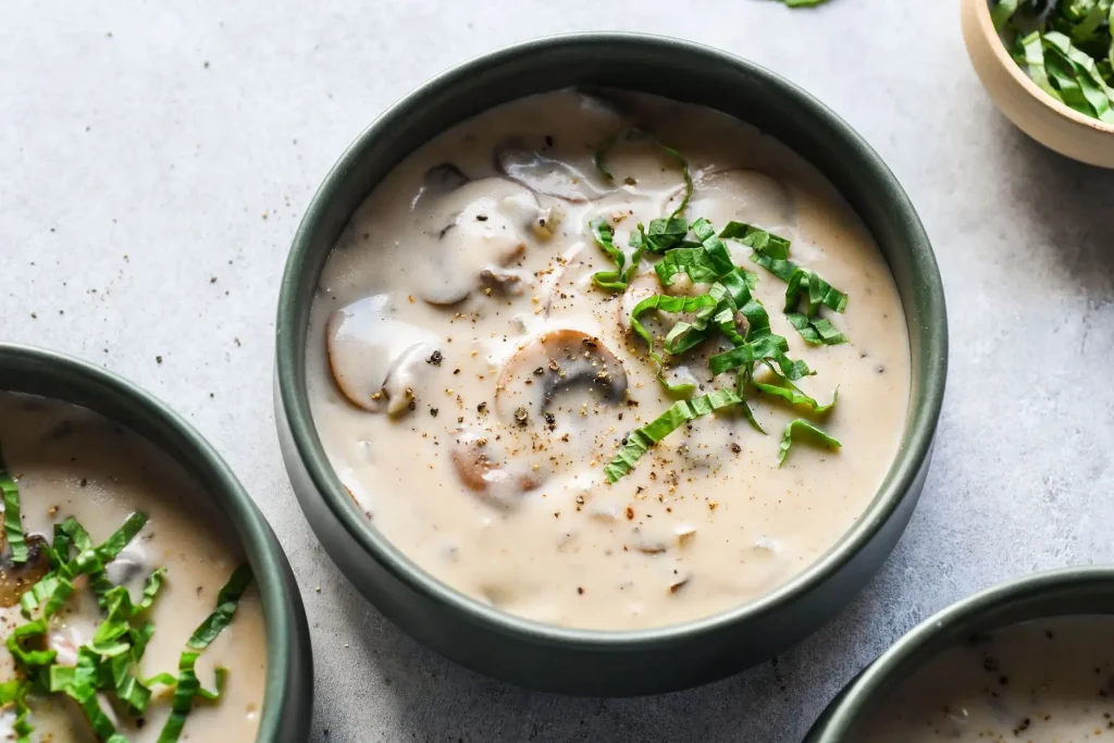 A close-up of a bowl of creamy mushroom soup, garnished with fresh herbs and black pepper