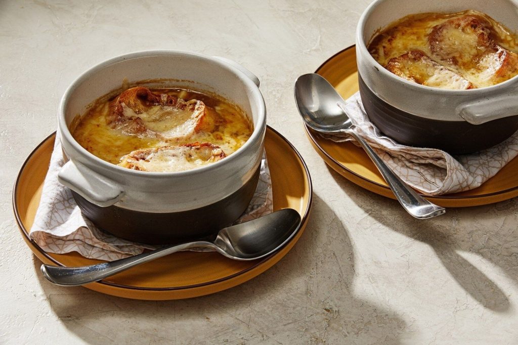 Two-bowls-of-classic-French-onion-soup-with-croutons-and-melted-cheese-on-a-light-background.