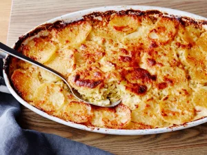 Close-up-of-a-creamy-potato-gratin-freshly-baked-in-a-white-oval-dish,-a-spoon-scooping-a-serving.