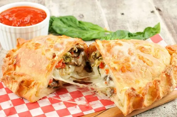 Calzone stuffed with melted cheese and vegetables, cut open with tomato sauce