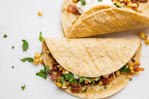 Soft burrito filled with corn, cilantro, and sour cream, displayed on a white background