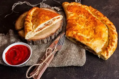 Half-sliced calzone with a bowl of tomato sauce on a rustic surface