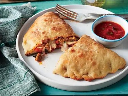 Homemade calzone served with a side of tomato dip on a white plate