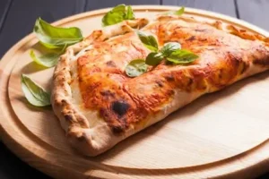 Traditional Italian calzone topped with fresh basil leaves on a wooden board