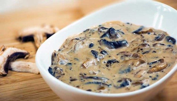 Close-up-of-creamy-mushroom-sauce-in-a-white-bowl-with-mushrooms-nearby