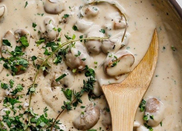 Close-up-view-of-creamy-mushroom-sauce-in-pan-with-herbs-and-wooden-spoon