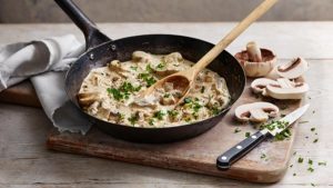 Creamy-mushroom-sauce-in-pan-with-spoon-and-mushrooms-on-cutting-board