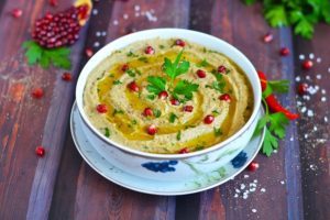 A bowl of Lebanese Mutabbal dip garnished with pomegranate seeds and parsley, served with olive oil.