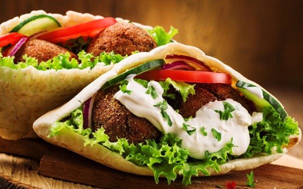 Middle Eastern falafel sandwich with crispy falafel balls, pickled vegetables, fresh herbs, and creamy tahini.