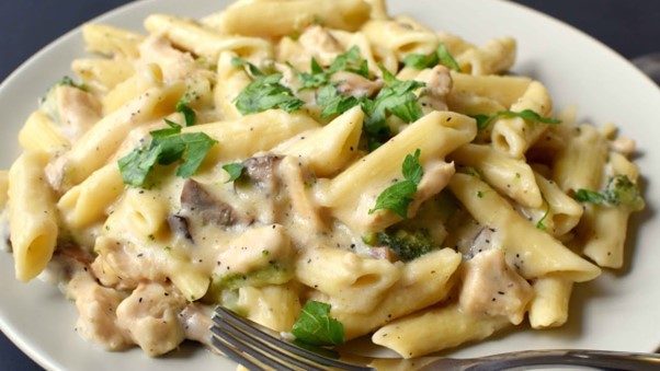 Rich and creamy chicken Alfredo pasta with mushrooms and parsley, served on a white plate with a fork