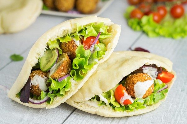 Golden-brown crispy falafel served on a wooden board with tahini dipping sauce and fresh parsley.