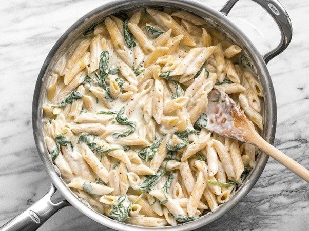 Creamy penne Alfredo pasta with artichokes, red onions, and fresh herbs, served on a white plate