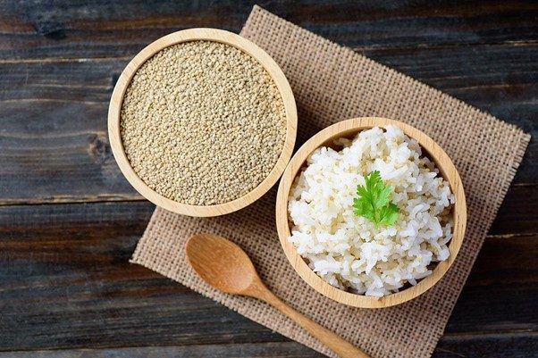 A rustic wooden bowl filled with tri-color quinoa grains, with a wooden spoon resting on a wooden surface